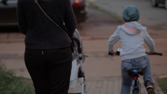 Mutter-mit-zwei-Kindern-auf-der-Straße.-Älterer-Junge-mit-dem-Fahrrad