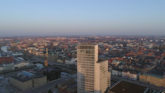 Drone-shot-flying-down-by-modern-skyscraper-office-buildings-in-Malmö-city,-Sweden.-Aerial-view-of-Malmoe-cityscape-skyline-at-sunset
