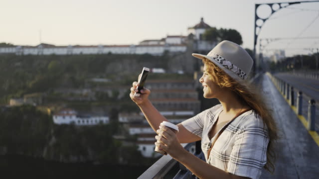 Lady-in-hat-and-dress-taking-selfie-on-bridge
