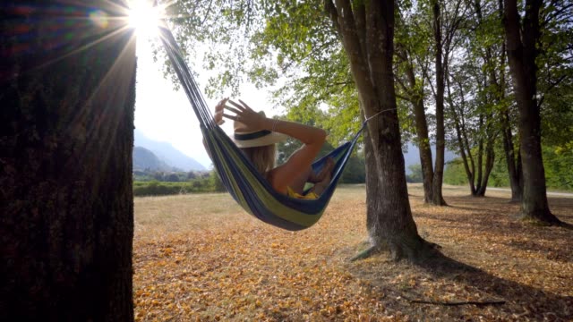 Serene-young-woman-relaxing-on-hammock-at-sunset-enjoying-nature-in-late-Summer.-People-travel-enjoying-freedom-and-peaceful-environment---slow-motion