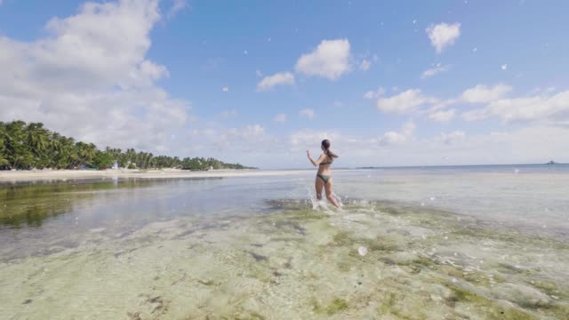 Joyful-young-woman-in-swimsuit-running-on-sea-water-on-summer-beach