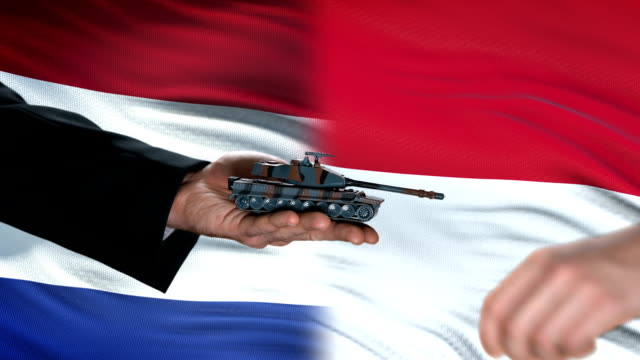 Netherlands-and-Indonesia-officials-exchanging-tank-for-money,-flag-background