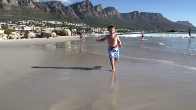 Junge-läuft-in-Richtung-der-Kamera-am-Strand,-Südafrika