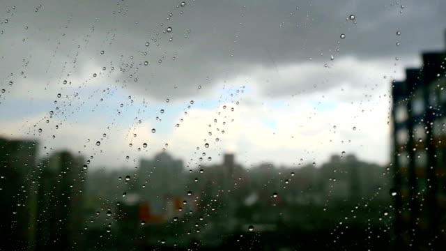 Urban-view-of-rain-drops-falls-on-a-window-during-a-stormy-day-overlooking-city-skyline-in-the-background