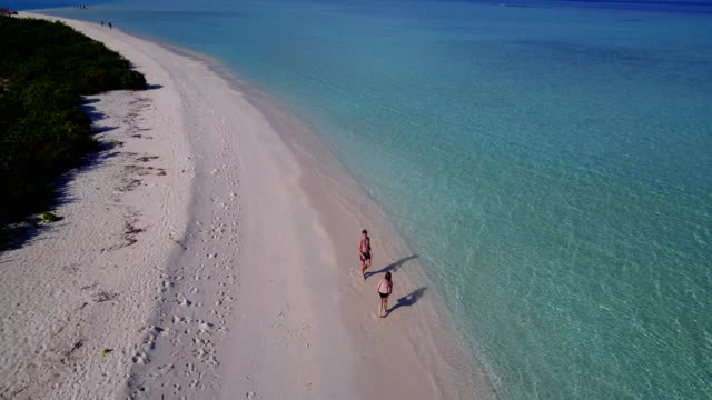 v03813-Aerial-flying-drone-view-of-Maldives-white-sandy-beach-on-sunny-tropical-paradise-island-with-aqua-blue-sky-sea-water-ocean-4k-2-people-young-couple-man-woman-playing-ball-fun-together