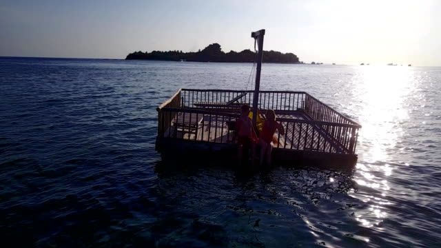 v03839-fliegenden-Drohne-Luftaufnahme-der-Malediven-weißen-Sandstrand-2-Personen-junges-Paar-Mann-Frau-entspannend-auf-sonnigen-tropischen-Inselparadies-mit-Aqua-blau-Himmel-Meer-Wasser-Ozean-4k-schwimmenden-Ponton-Steg-Sonnenbaden-zusammen