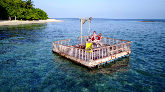 v03840-fliegenden-Drohne-Luftaufnahme-der-Malediven-weißen-Sandstrand-2-Personen-junges-Paar-Mann-Frau-entspannend-auf-sonnigen-tropischen-Inselparadies-mit-Aqua-blau-Himmel-Meer-Wasser-Ozean-4k-schwimmenden-Ponton-Steg-Sonnenbaden-zusammen