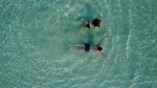 v04199-Aerial-flying-drone-view-of-Maldives-white-sandy-beach-2-people-young-couple-man-woman-swimming-splashing-underwater-on-sunny-tropical-paradise-island-with-aqua-blue-sky-sea-water-ocean-4k