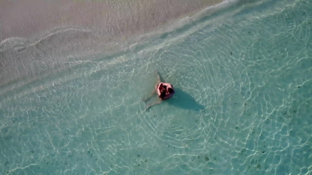 v04190-Aerial-flying-drone-view-of-Maldives-white-sandy-beach-2-people-young-couple-man-woman-swimming-splashing-underwater-on-sunny-tropical-paradise-island-with-aqua-blue-sky-sea-water-ocean-4k