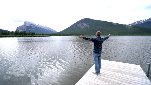 Hombre-joven-de-brazos-extendidos-en-el-muelle-del-lago,-Canadá