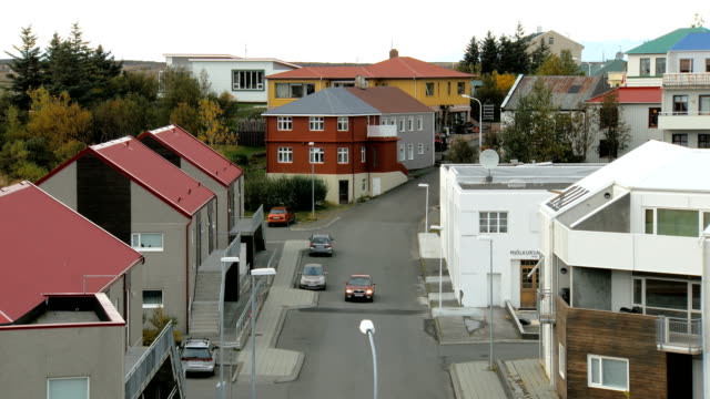 kleine-isländische-Straße-mit-Häusern,-Auto-geparkt-in-Herbsttag,-ein-rotes-Auto-bewegt-sich