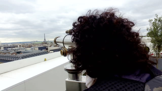 Tourist-woman-enjoy-Paris-cityscape-view-with-coin-binocular-telescope-at-top-terace-balcony-in-Galery-Lafayette