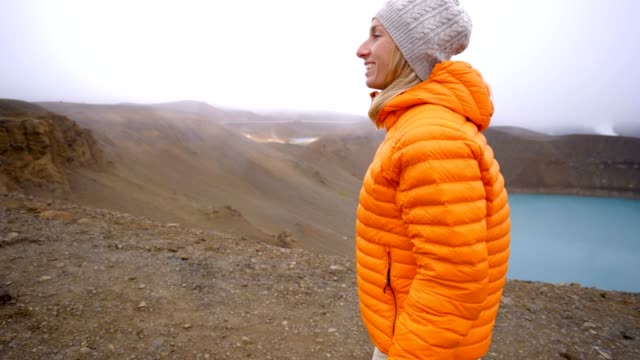 Young-woman-in-Iceland-contemplating-crater-lake-from-top-of-it,-Springtime.-People-travel-carefree-lifestyles-concept--4K-video