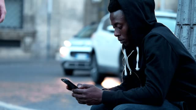 nachdenklich-junge-afrikanische-Amerikaner-mit-Smartphone-sitzen-auf-der-Straße