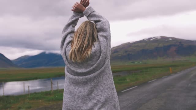 Happy-young-woman-walking-on-asphalt-road-in-Iceland-and-having-some-fun,-enjoying-view.-Slow-motion,-cinematic-shot