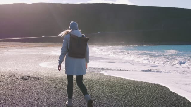 Tourist-Frau-mit-Leder-Rucksack-zu-Fuß-in-der-Nähe-der-Küstenlandschaft-in-Island,-Zeitlupe,-filmische-erschossen