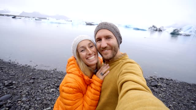 4-K-Video-de-pareja-de-jóvenes-que-se-divierten-tomando-selfie-en-el-lago-de-glaciar-en-la-laguna-Jokulsarlon-en-Islandia.-Dos-personas-viajan-romance-amor-compartir-el-concepto-de-comunicación-de-estar-juntos.-Primavera,-las-temperaturas-frías