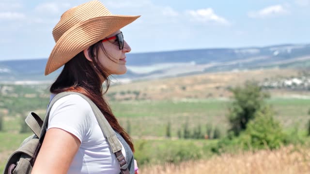 Side-view-portrait-of-young-backpack-woman-in-hat-and-sunglasses-enjoying-amazing-natural-landscape
