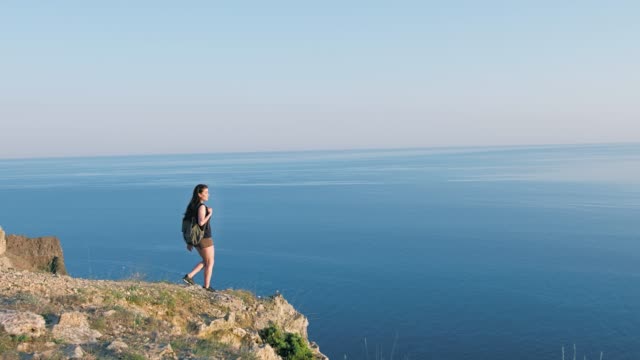 Active-backpacker-female-traveler-approach-to-dangerous-break-of-high-cliff-extreme-long-shot