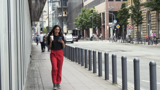 Junge-Frau-zu-Fuß-auf-Bürgersteig-trinken-Kaffee-aus-einem-Pappbecher