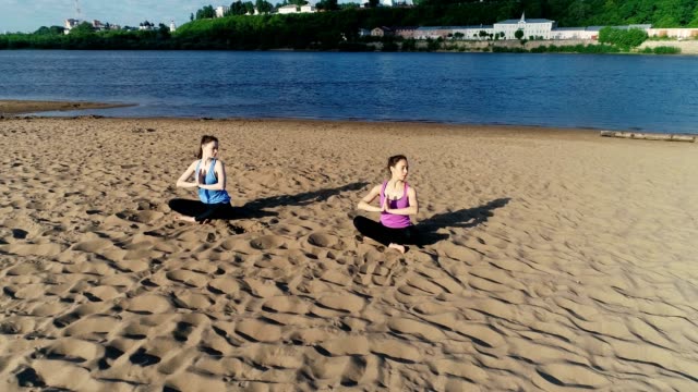 Zwei-Frauen-Yoga-am-Sandstrand-des-Flusses-erstreckt.-Blick-auf-die-schöne-Stadt.