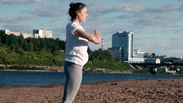 Woman-stretching-yoga-on-the-beach-by-the-river-in-the-city.-Beautiful-city-view.