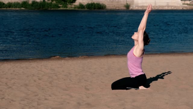 Woman-stretching-yoga-on-the-beach-by-the-river-in-the-city.-Beautiful-city-view.-Breathing-exercise.