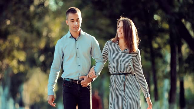 Young-couple-walking-along-the-city-park-together,-go-to-the-camera