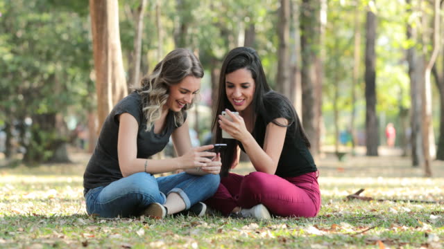 Amigos-cándidos-fuera-en-el-parque-de-comprobación-de-sus-teléfonos-móviles.-Chicas-sentadas-mirando-sus-smartphones