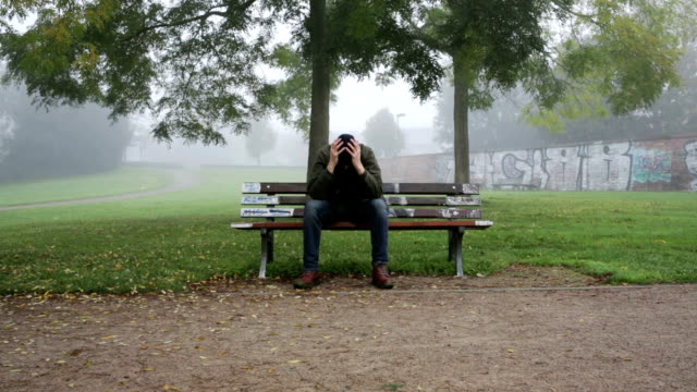 man-expressing-sorrow-on-bench-in-park