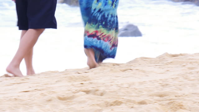 An-older-couple-holding-hands-and-walking-down-the-beach,-starting-close-up-on-their-feet