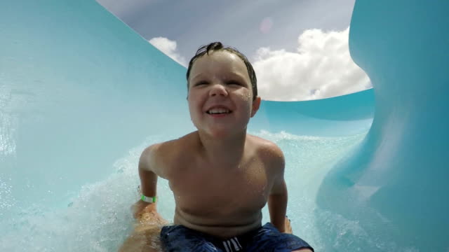 Happy-young-boy-going-down-curved-waterslide-in-slow-motion