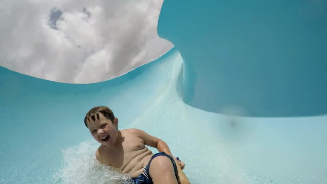Happy-young-boy-going-down-curved-waterslide-in-slow-motion