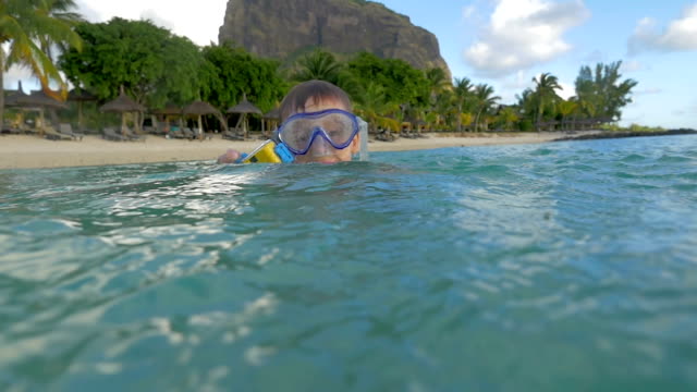 Slow-motion-view-of-small-boy-swimming-in-the-Indian-Ocean-in-the-snorkeling-mask-and-take-a-picture,-Port-Louis,-Mauritius-Island