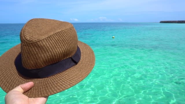 Mano-que-sostiene-el-sombrero-Panamá-de-vacaciones-con-vistas-al-paraíso