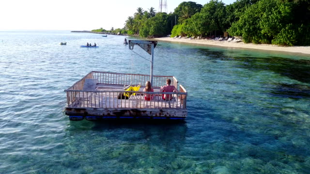 v03843-fliegenden-Drohne-Luftaufnahme-der-Malediven-weißen-Sandstrand-2-Personen-junges-Paar-Mann-Frau-entspannend-auf-sonnigen-tropischen-Inselparadies-mit-Aqua-blau-Himmel-Meer-Wasser-Ozean-4k-schwimmenden-Ponton-Steg-Sonnenbaden-zusammen