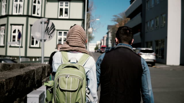 Back-view-of-young-stylish-couple-walking-in-downtown-together.-Man-and-woman-holding-hands-and-exploring-the-city
