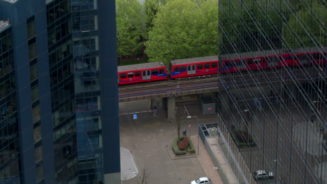 Tram-Between-Buildings,-Dlr-Train,-Financial-Ticker,-Canary-Wharf,-London
