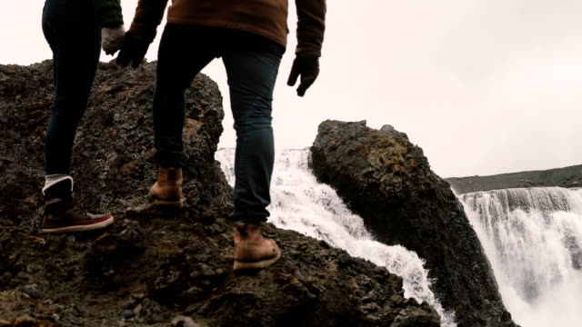 Junger-Mann-und-Frau,-stehend-auf-einem-Hügel-nach-Wandern-und-auf-einem-mächtigen-Wasserfall-in-Island,-berühmte-Sehenswürdigkeit-suchen