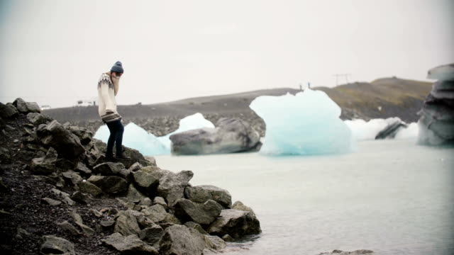 Young-attractive-woman-in-lopapeysa-standing-in-ice-lagoon.-Tourist-exploring-the-famous-sight-of-Iceland-alone