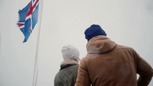 Back-view-of-young-couple-traveling-on-the-ship-with-Icelandic-flag-together.-Man-and-woman-look-on-sea-together