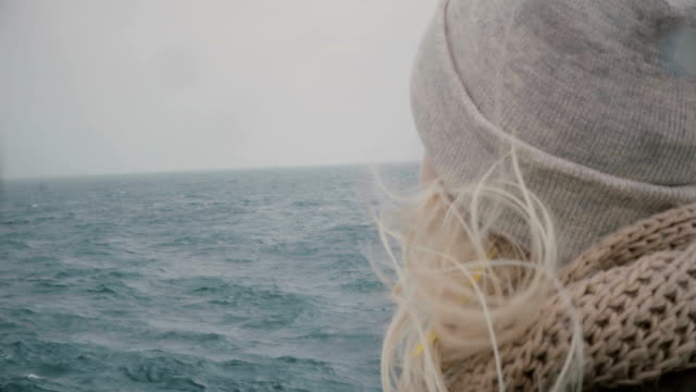 Close-up-view-of-young-blonde-woman-traveling-on-ship.-Attractive-female-looking-on-sea-and-waves,-hair-waving-on-wind