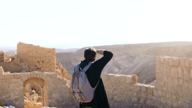 European-man-takes-photos-of-ancient-scenery.-Male-tourist-with-camera-and-backpack-explores-mountain-ruins.-Israel-4K
