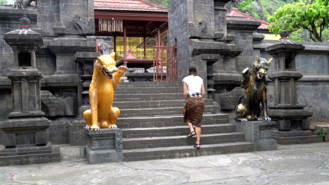 Eine-Frau-in-einem-langen-Rock-steigt-auf-einen-buddhistischen-Tempel-auf-eine-Steintreppe-mit-Statuen