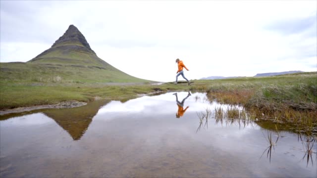 Junge-Frau-in-Island-über-Fjord-Fluss-am-berühmten-Berg-Kirkjufell-springen