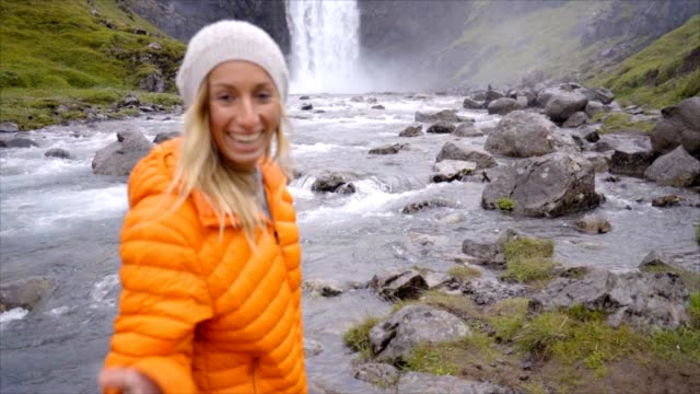 Follow-me-to-the-waterfall-young-woman-waving-at-boyfriend,-girlfriend-leading-man-to-falls-in-Iceland-People-travel-concept--Slow-motion