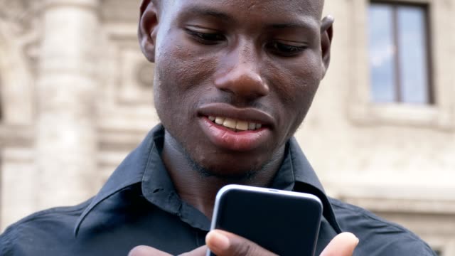 Lächelnd-amerikanischen-afrikanischen-jungen-Mann-auf-seinem-Smartphone-im-freien-Eingabe