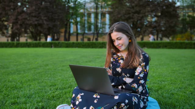 Atractivo-guapa-joven-usando-la-laptop-en-el-parque-al-aire-libre