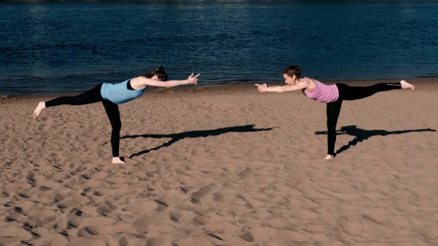 Two-woman-doing-yoga-on-the-beach-by-the-river-in-the-city.-Beautiful-view.