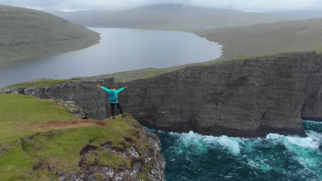 AERIAL:-Woman-on-hiking-trip-outstretches-arms-after-walking-up-to-edge-of-cliff